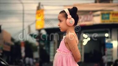 一个<strong>可爱</strong>的孩子站在路边的肖像，一个穿着粉色连衣裙和粉色耳机的<strong>可爱</strong>的小<strong>可爱</strong>女孩